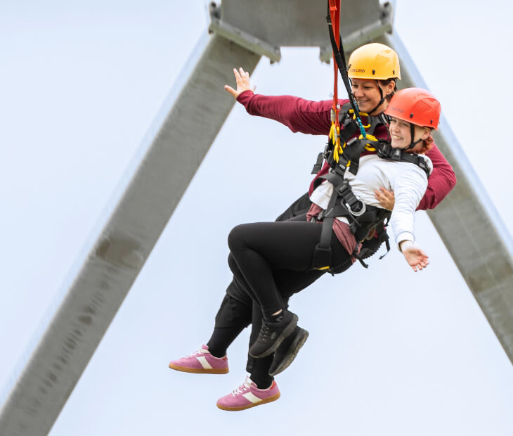 Zwei Freunde klammern sich beim Tandem Giantswing aneinander und lachen