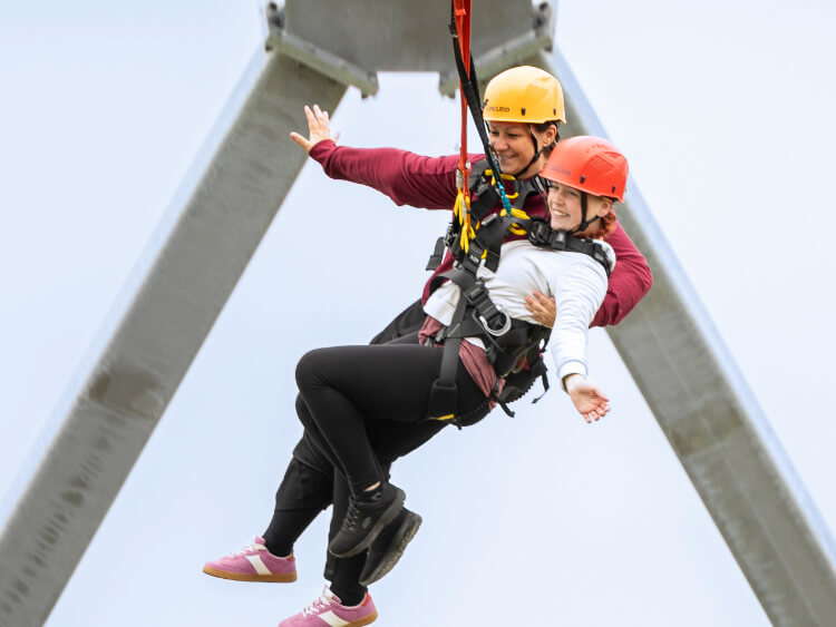 Zwei Freunde klammern sich beim Tandem Giantswing aneinander und lachen